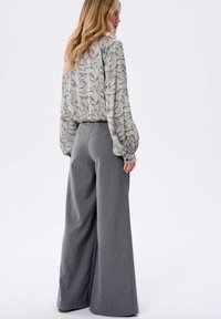 Lichtgrijze, wijde broek in combinatie met een gebloemde blouse met een bladdessin. De blouse heeft pofmouwen en een losse pasvorm.