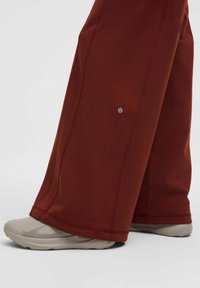 Széles lábú, könnyű nadrág sötétvörös szövetből, látható varrással és logó részlettel. Világosszürke sportcipővel párosítva.