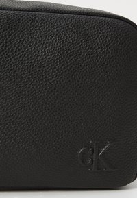 Black leather cosmetic bag with a textured finish and embossed "CK" logo. Features a rectangular shape and smooth zipper closure.