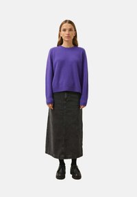 Lila gestrickter Pullover mit gerippten Bündchen, kombiniert mit einem schwarzen Jeans-Maxirock und schwarzen Schnürschuhen. Einfaches, lässiges Design.