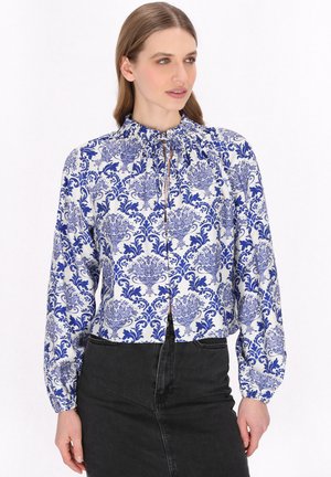 Bluză cu model albastru și alb, cu decolteu strâns și mâneci lungi, având un design floral dintr-un material neted. Asortată cu o fustă neagră.