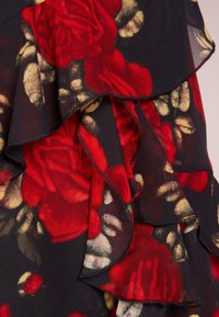 Tissu noir avec un motif floral de roses rouges et jaunes. Comprend des volants superposés avec une finition douce et texturée et des coutures à bords bruts.