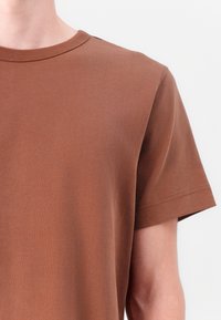 Bruine T-shirt met korte mouwen en een ronde hals, gemaakt van zachte stof. Zichtbare stikdetails en een clean, minimalistisch ontwerp.