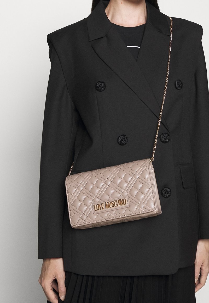 Prošívaná béžová kabelka se zlatými kovovými doplňky, s logem "LOVE MOSCHINO". Dokončena řetízkovým popruhem a texturovanou látkou.