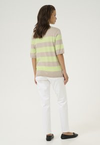 Lichte beige trui met brede groene strepen, korte mouwen. Gecombineerd met witte broek en zwarte ballerina's, model staat met de rug naar de camera.