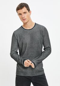 Maglietta a maniche lunghe a righe bianche e nere con scollatura tonda e rifiniture a contrasto bianche sul collo e sui polsini, caratterizzata da un design a maglia testurizzata.