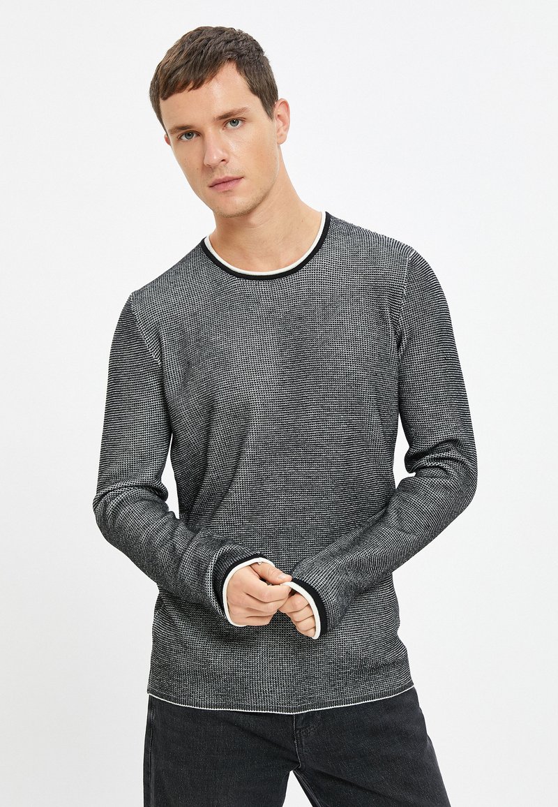 Maglietta a maniche lunghe a righe bianche e nere con scollatura tonda e rifiniture a contrasto bianche sul collo e sui polsini, caratterizzata da un design a maglia testurizzata.