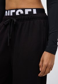 Melnas sporta bikses ar elastīgu jostu un izcelto baltu "DIESEL" logotipu. Mīksts audums un regulējama aukliņa detaļa.