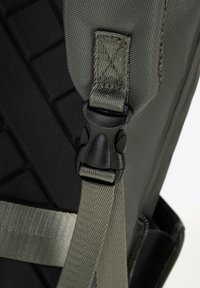 Zwarte rugzakband van een gestructureerde, geweven stof met een plastic gesp. De band is olijfgroen met een gladde afwerking en platte webbing.