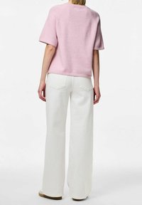 Světle růžový svetr s krátkým rukávem a texturovaným povrchem, kombinovaný s vysokými bílými kalhotami s širokými nohavicemi, které mají detaily na zadních kapsách.