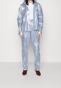 Giacca e pantaloni metallici di colore blu chiaro, caratterizzati da una texture lucida e una vestibilità rilassata. Completati da una maglietta bianca e scarpe con tacco bordeaux.