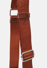 Oranssi kangashihna, jossa on kohokuvioitu "Valentino"-logo, teksturoitu ruskea korostus ja hopeanväristä metallia oleva säätömekanismi.