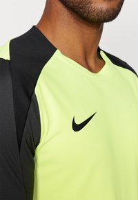 Hombre vistiendo una camiseta deportiva de Nike en negro y amarillo neón, mostrando el pecho y el cuello con el logotipo de swoosh de Nike visible en el lado izquierdo.