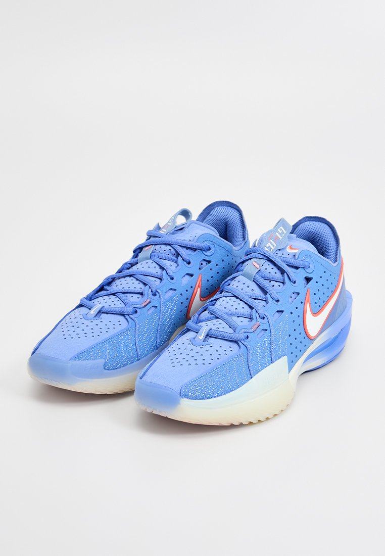 Zapatillas deportivas azules con parte superior de malla, diseño perforado y un distintivo swoosh de Nike en rojo. Cuentan con una suela acolchada y cierre de cordones.