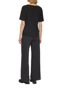 Chemise noire en coton à manches courtes avec une coupe décontractée, associée à un jean large taille haute en charbon ; les deux présentent une texture lisse.