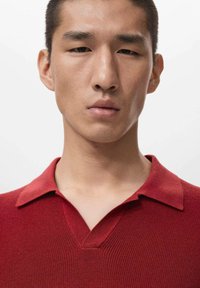 Rød strikket polo med V-hals og korte ærmer; har en tekstureret finish og ensfarvet uden mønstre eller accenter.