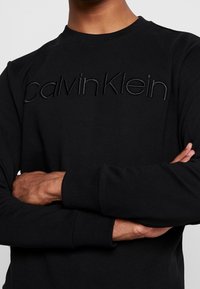 Felpa nera con il logo ricamato "Calvin Klein" nello stesso colore. Presenta un collo rotondo e polsini a coste. Tessuto morbido.