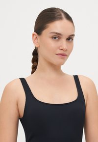 Svart ribbestrikket stoff topp med firkantet hals og tynne stropper. Glatt tekstur, tettsittende design, passer til uformell bruk eller som lag-på-lag.