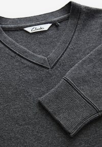Sivý sveter s výstrihom do V, s rebrovanými manžetami a lemom. Mäkká, textúrovaná látka s viditeľným prešitím a štítkom označeným "Clarks".