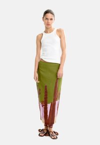 Zielona lniana spódnica z nadrukiem kaktusów i kwiatów, połączona z białym dopasowanym topem na ramiączkach i czarnymi sandałami z frędzlami.