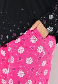 Černý top s dlouhými rukávy, zdobený stříbrnými a růžovými vzory hvězd, kombinovaný s růžovými kalhotami, které mají bílé sněhové vločky a černé akcenty.