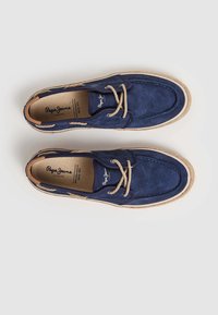 Zapatillas náuticas de ante azul marino con un cordón de cuerda beige, suela de goma y detalles cosidos; forradas con material beige; logo de la marca en el interior.