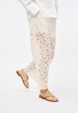 Pantaloni larghi in pizzo color crema con motivi floreali. Sandali beige con una cinghia texture e un dettaglio con fibbia rotonda.