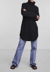 Svart ribbad polotröja med långa ärmar, kombinerad med ljusblå vida jeans och svarta slip-in sandaler.