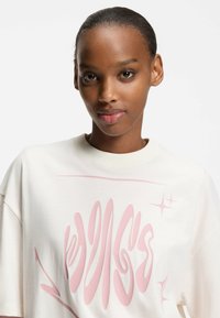 Hvid bomulds-T-shirt med stort pink grafisk motiv på forsiden, korte ærmer og rund halsudskæring. Glat tekstur.