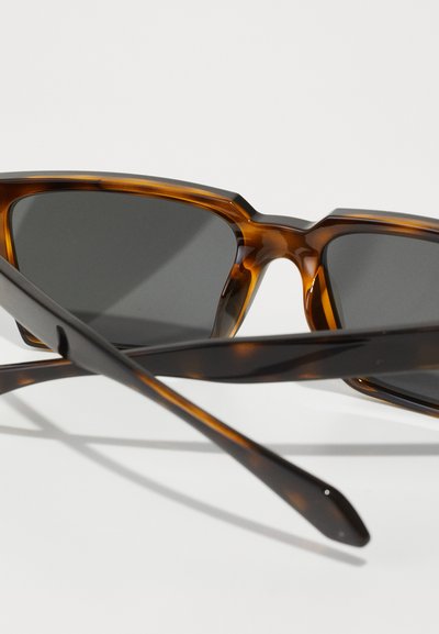 Brown tortoiseshell sunglasses with angular frames and dark lenses, featuring thin arms that curve slightly at the tips.