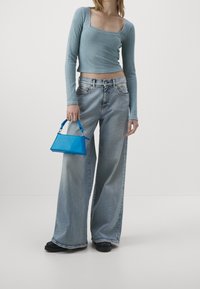 Ljusblå, ribbad långärmad topp med kvadratisk halsringning, tillsammans med vida, urtvättade jeans. Accessoar: liten, glansig blå rektangulär handväska.