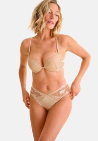 Reggiseno color beige in pizzo e slip abbinati con ricami floreali, pannelli trasparenti e spalline regolabili, progettati per una vestibilità liscia e confortevole.