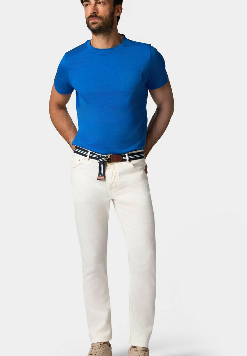 Modrá bavlněná trička s krátkým rukávem a kapsou na hrudi, spojená s bílými džíny a páskem s námořnickým pruhem a hnědou sponou.