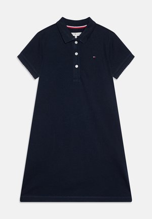 Marineblå polokjole med korte ærmer, krave, tre hvide knapper og lille broderet logo på brystet.