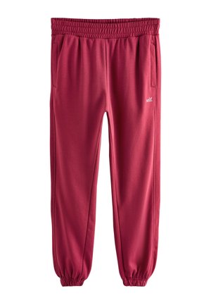Pantaloni de trening roșii cu talie și manșete elastice, buzunare laterale și text alb mic „self.” pe partea superioară a coapsei.