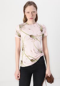Camiseta de manga curta rosa com um padrão floral em verde e roxo. O tecido parece suave; a camiseta é ligeiramente franzida na cintura.