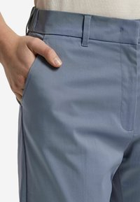 Ljusblå byxor gjorda av slät tyg, med en sidoficka och en platt front. Midjan är strukturerad med bälteslänkar.