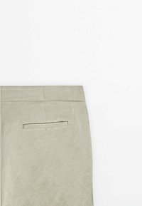 Tissu beige clair avec une poche fendue horizontale et des coutures visibles près du bord supérieur sur un fond uni.