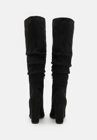 Botas negras largas hasta la rodilla hechas de suave ante, con un diseño holgado, tacones cuadrados altos y cremalleras laterales para facilitar su uso.