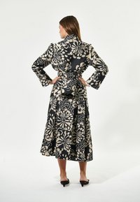 Kleid z obliko cvetja v črno-kremni barvni paleti, z dolgimi rokavi, pasom na vezanje ter ohlapno krilo, ki sega pod kolena.