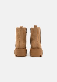Botines tobilleros marrones con acabado de ante, que cuentan con una suela gruesa, cremalleras laterales y tiradores para ponerse con facilidad. Diseño minimalista, sin patrones visibles.