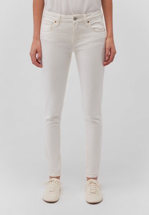 White skinny jeans with a smooth texture, front pockets, and subtle copper-tone hardware, paired with light beige lace-up shoes.