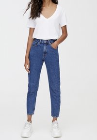 Vit V-ringad t-shirt, blå jeans med hög midja, uppvikta vid anklarna, kombinerade med vita sneakers. Ren, avslappnad stil med minimala detaljer.