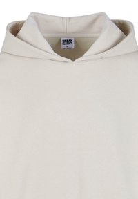 Beige kapucnis pulóver kenguruzsebbel, puha anyagból, rögzített kapucnival, és egy címkével belül. Sima textúra minimalista dizájnnal.