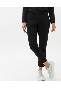 Pantalons noirs fuselés avec une texture lisse, dotés d'un devant plat, de passants de ceinture et d'une coupe à la cheville, associés à des baskets blanches de sport.