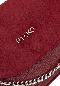 Borsa a tracolla rossa in suede e pelle con una accentuazione in catena argentata, caratterizzata da una forma tondeggiante e un logo impresso. Texture liscia e colore intenso.