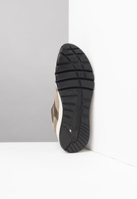 Wildlederschuhe mit einer schwarzen Gummisohle, die über ein markantes Sohlenprofil verfügt. Die Farbe ist beige mit Akzenten und einem Logodetail.