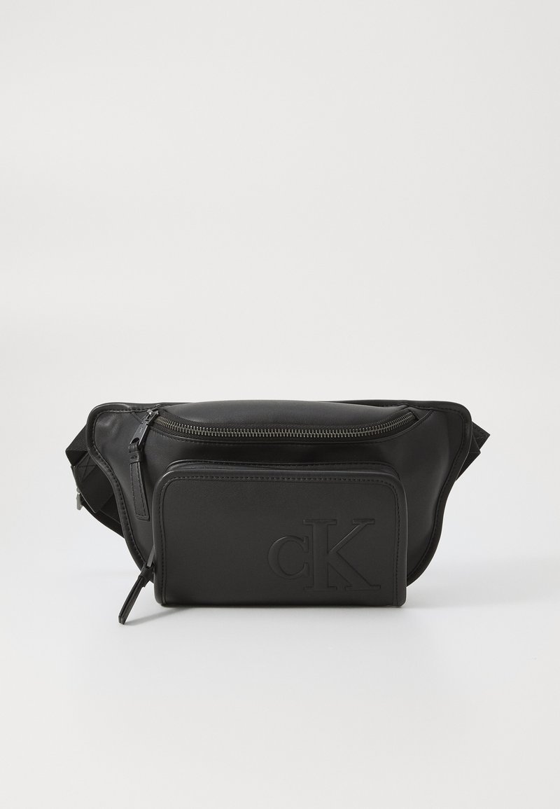 Zwarte leren heuptas met een ritsvak, voorkant vak, geperst "cK" logo en verstelbare strap. Soepele textuur en slank ontwerp.