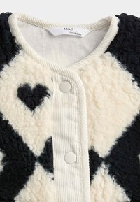 Fleecejakke med et diamantmønster i creme og marineblå, med en lille hjerte detalje, kordfløjl kant og trykknap lukning.