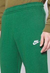 Green Nike sweatpants made of soft fabric, featuring an elastic waistband and white logo on the right leg. Smooth texture and straight fit.